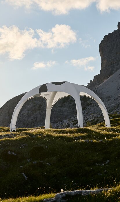 Inflatable tent in the mountains White inflatable tent with printed roof on a rocky meadow, with soft backlighting